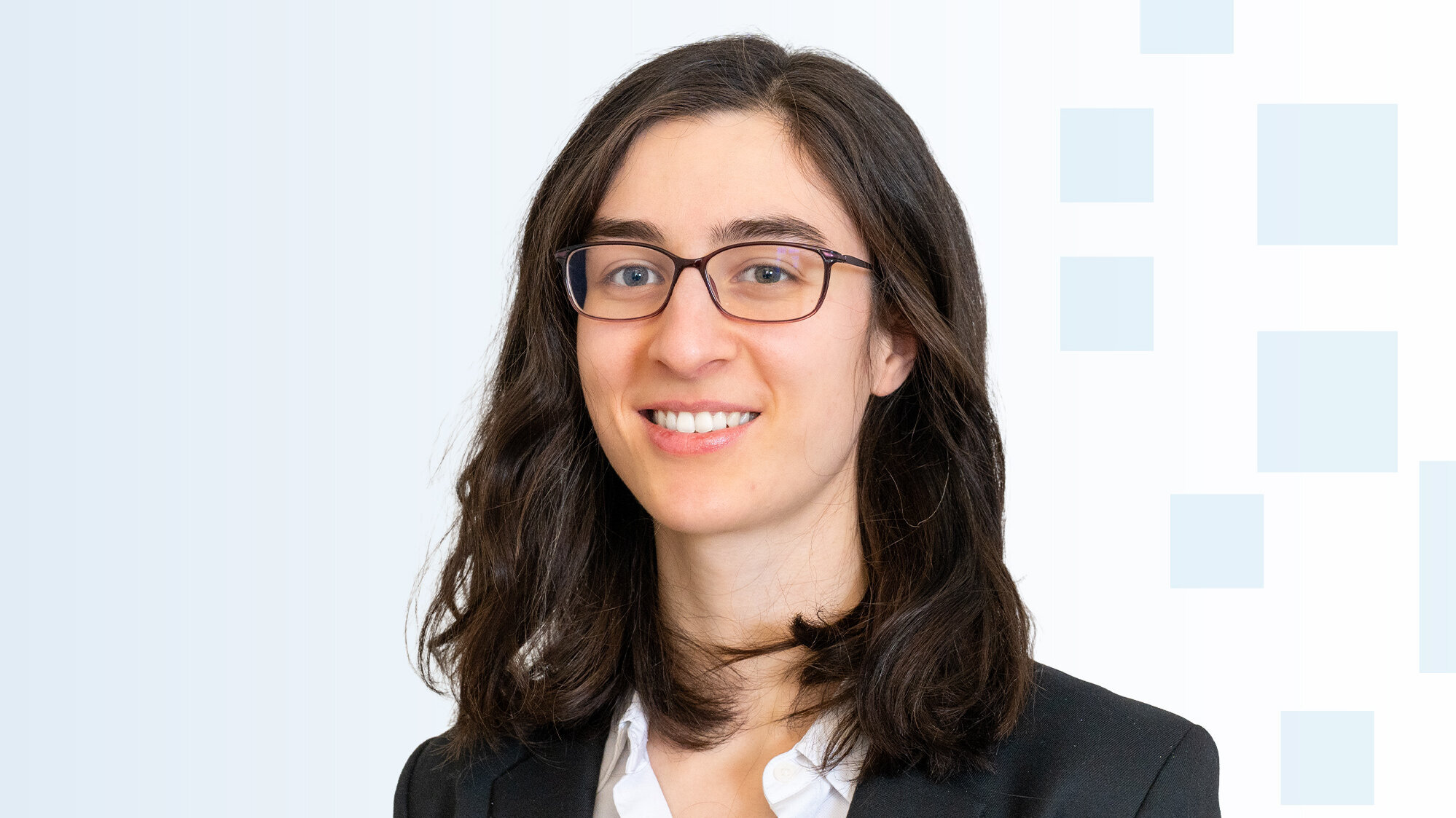 Eine Frau mit langen, dunklen Haaren und einer schwarzenjacke lächelt in die Kamera. Sie trägt eine weiße Bluse und Brillen. Der Hintergrund ist hell und grafisch strukturiert, mit sanften, abgestuften Farben.
