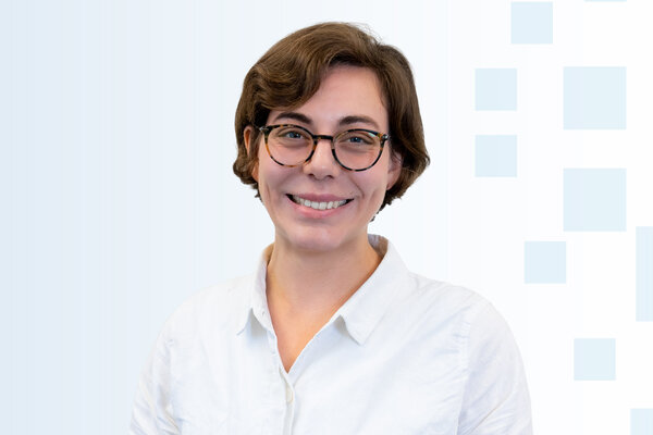 Ein Porträt einer lächelnden Person mit braunem, lockigem Haar und Brille. Sie trägt ein weißes Hemd und hat einen freundlichen Ausdruck. Der Hintergrund ist in sanften Blau- und Grautönen gehalten.